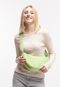 Borsa a tracolla verde in tessuto, dalla forma arrotondata e con una tracolla larga, caratterizzata da una texture liscia e un design minimalista.