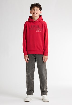 Felpa rossa con logo stampato grigio, dotata di cappuccio con cordino. Abbinata a jeans in denim grigio e sneakers bianche.