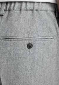 Gray wool-blend pants with a textured surface, featuring a black button closure and horizontal pocket detail at the back.