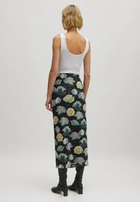 Bloemenrok van donkere stof met een patroon van groene en gele rozen. Gepaard met een witte tanktop en zwarte knielange laarzen.