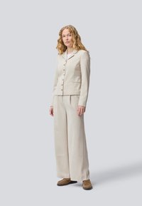 Beige skräddarsydd blazer med kilar och fem knappknäppningar, matchad med vida beige byxor. Strukturerad tyg med slät ytfinish.