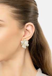 Gold-tone floral earrings with textured petals and subtle shimmer, featuring a secure backing, worn on a model's ear.