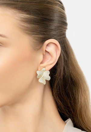Gold-tone floral earrings with textured petals and subtle shimmer, featuring a secure backing, worn on a model's ear.