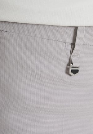 Pantalones gris claro con textura, combinados con una blusa blanca, que cuentan con un pequeño llavero de metal y negro sujeto a una presilla del cinturón.
