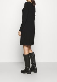 Schwarzes Strickkleid mit langen Ärmeln und seitlichen Schlitzen. Kombiniert mit knielangen schwarzen Lederstiefeln mit einem robusten Absatz. Einfaches Design.