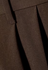 Tissu marron avec une surface texturée et un léger éclat, présentant des plis et des pliures soigneusement repassés pour un aspect sur mesure.