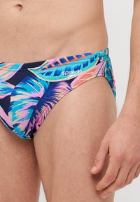Chiloane de înot Speedo, cu un imprimeu vibrant de frunze tropicale în nuanțe de albastru, roz și verde pe un fundal închis; talie elastică; textură de țesătură netedă.