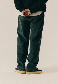 Σκούρο πράσινο, φαρδύ παντελόνι από βαρύ ύφασμα, με λεία υφή. Συνδυασμένο με μαύρα παπούτσια με ανοιχτόχρωμη σόλα.