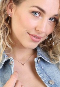 Zilveren V-vormige oorbellen en een bijpassende V-vormige ketting. Model met een spijkerjack en zachte golven in het haar. Close-up van de sieraden.