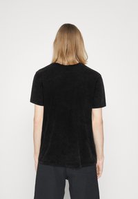 Camiseta negra de manga corta, textura suave, escote redondeado, corte relajado, diseño liso, sin patrones o acentos visibles.