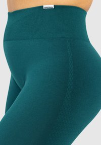 Türkisblaue High-Waist-Leggings mit geripptem Bund, glatter Textur und dezenten Nähten, geeignet für Sportbekleidung.