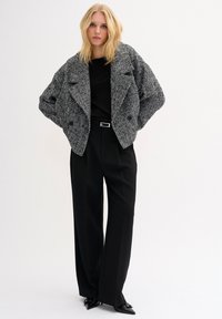 Juoda ir balta houndstooth rašto striukė su per dideliu siluetu, dviem priekinių kišenėmis, derinama su juodomis kelnėmis ir smailiais juodais batais.