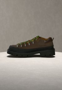 Chaussure de randonnée marron avec une semelle noire épaisse et des lacets verts et jaunes colorés sur fond neutre.