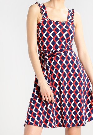Rood-wit-blauw gestippelde mouwloze jurk met een vierkante halslijn, ruches op de schouderbanden en een strik in de taille, met een uitlopende rok.