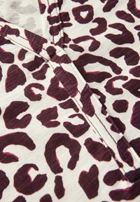 Tela de estampado de leopardo con grandes manchas de burdeos oscuro sobre un fondo claro, con una textura suave y detalles de costura visibles.