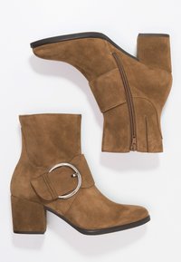 Botas de tobillo de ante marrón con puntera cuadrada, tacón cuadrado, cremallera lateral y un acento de hebilla circular en la correa.