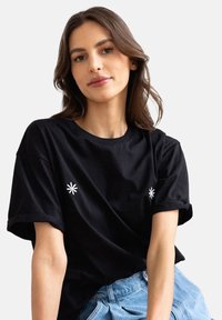 Czarna bawełniana koszulka z krótkim rękawem, okrągłym dekoltem i białymi haftami kwiatowymi z przodu.