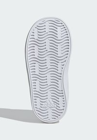 Bílá podrážka tenisky s vlnitým vzorem, textura povrchu a zubaté okraje. Obsahuje malé logo Adidas blízko paty.