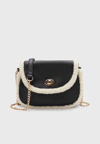 Svart axelväska med krämfärgad fårskinnsdetalj, guldfärgad vändlås och guldkedjehandtag på en enkel ljusgrå bakgrund.