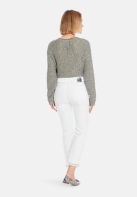 Leichtgewichtiger, olivgrüner, verkürzter Strickpullover mit lockerer Maschenbindung. Kombiniert mit eng anliegenden weißen Jeans und metallischen Ballerinas. Rückansicht.