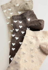 Set di tre paia di calzini a cotone colore beige, marrone e beige chiaro, con piccoli cuori bianchi su un tessuto texturizzato.
