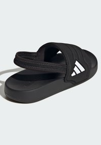 Černé pantofle se strukturovaným textilním svrškem a tvarovanou gumovou podrážkou. Jsou doplněny bílým logem a širokými nastavitelnými pásky.