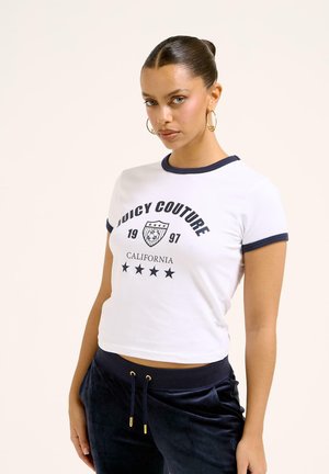 Bijela skraćena majica s plavim detaljima na rubovima, s natpisom "Juicy Couture", grafikom štita i pet zvjezdica ispod.