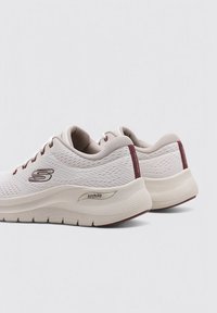 Zapatillas de malla blancas con acentos en burdeos, que cuentan con una suela texturizada gruesa y la marca "ArchFit" en el lateral para un soporte mejorado.