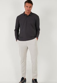 Polo de manga larga gris oscuro con cuello, combinado con pantalones beige claros ajustados y zapatillas negras. Textura de tejido suave, ajuste casual.