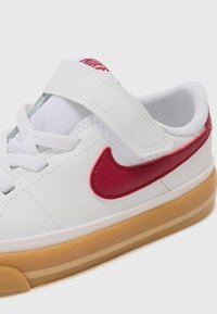Fehér sneaker sima bőr felső résszel, piros szintetikus betétekkel, tépőzáras pánttal és gumitalpazattal. Láthatóak a varrási részletek.