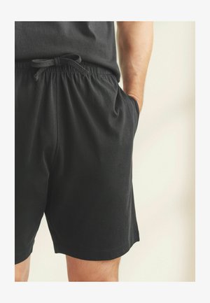 Shorts en coton noir avec une taille élastique et un cordon de serrage. Le tissu semble doux, avec des poches latérales et un design simple et épuré.