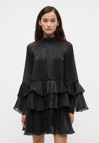 Must zwartne plekkide kleit pikade varrukatega, kõrge kaelusega, volangidega tasandite ja läbipaistva, tekstuuriga kangaga.