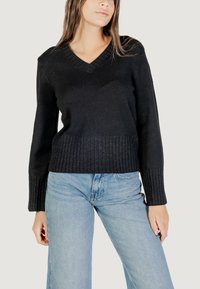 Maglione nero a maglia con scollo a V, orlo a costine e maniche lunghe. Abbinato a jeans in denim azzurri.