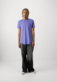 Paarse katoenen T-shirt met korte mouwen en een afgeronde zoom, gecombineerd met donkergrijze baggy jeans en zwart-witte sneakers.