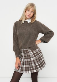 Brun ribbet genser med rund hals, kombinert med en plisserte rutete skjørt i brune, kremfargede og svarte nyanser. Modell med mørke strømpebukser.