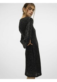 Robe noire en sequins avec des manches longues, silhouette ajustée etOurlet au niveau des genoux. Surface texturée avec des sequins scintillants pour un détail supplémentaire.