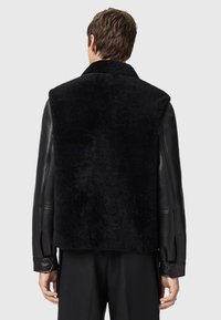 Black shearling jacket with leather sleeves; features a high collar, textured surface, and structured fit. Minimalist design and modern accents.