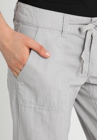 Jasnoszare lniane spodnie z regulowanym pasem na sznurek, bocznymi kieszeniami i luźnym krojem, z widocznymi przeszyciami i gładką fakturą.