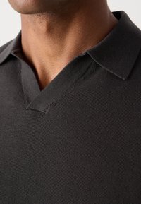 Tamno siva polo majica s dizajnom V-izreza, teksturiranom tkaninom i kontrastnim detaljima oko kragne. Približan pogled na izrez i područje ramena.