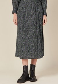 Schwarzer Midirock mit floralem Muster, der ein lila und grünes botanisches Design zeigt. Kombiniert mit schwarzen Schnürkampfstiefeln. Weicher, fließender Stoff.