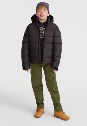 Zwarte pufferjack met horizontale stiksels, khaki cargo pants en tan boots. Model draagt een paarse beanie en een zwart sweatshirt eronder.