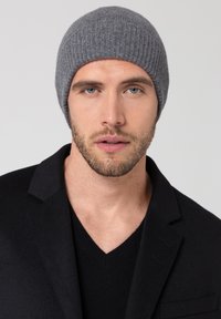 Grijze geribbelde gebreide beanie gemaakt van zacht materiaal, met een aansluitend ontwerp. Model draagt een zwarte blazer over een zwarte v-hals trui.