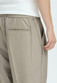 Grijze, lichte broek met een elastische tailleband, zijzakken en accentueeringen op de achterzak. Gladde textuur en subtiel weefpatroon.