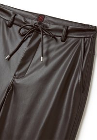 Pantalons en simili cuir noir avec taille à cordon, deux poches latérales et texture lisse. Présente des coutures minimales et une étiquette de marque.