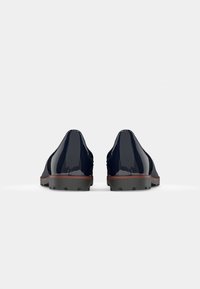 Marineblaue Lackleder-Schuhe mit abgerundeten Zehen, strukturierten schwarzen Gummisohlen und kontrastierenden braunen Akzenten. Minimalistisches Design mit glatter Oberfläche.