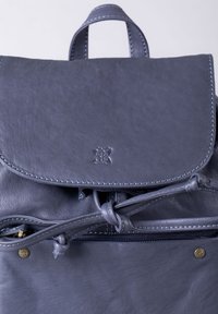 Leather backpack in dark gray with a rounded flap, contrasting stitching, and an exterior zip pocket. Features a subtle branded detail.