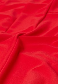 Rode stof met een gladde, glanzende textuur, met zachte draping en subtiele plooien, die de levendige kleur en de egale oppervlakte benadrukken.