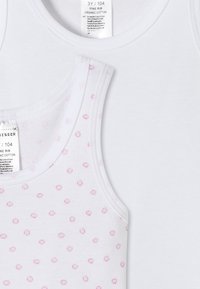 Två barnens linnen: ett i solid vitt, det andra vitt med rosa prickmönster. Båda gjorda av ekologisk bomull med ribbad textur.