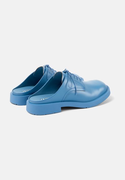 Scarpe slip-on in pelle blu con punta arrotondata, dettagli in pizzo e una spessa suola in gomma. Texture liscia con rivestimento interno.