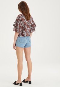 Haut à manches courtes à motifs avec un design à volants dans des tons terre, associé à un short en denim et des sandales noires à talons. Texture lisse, look décontracté.